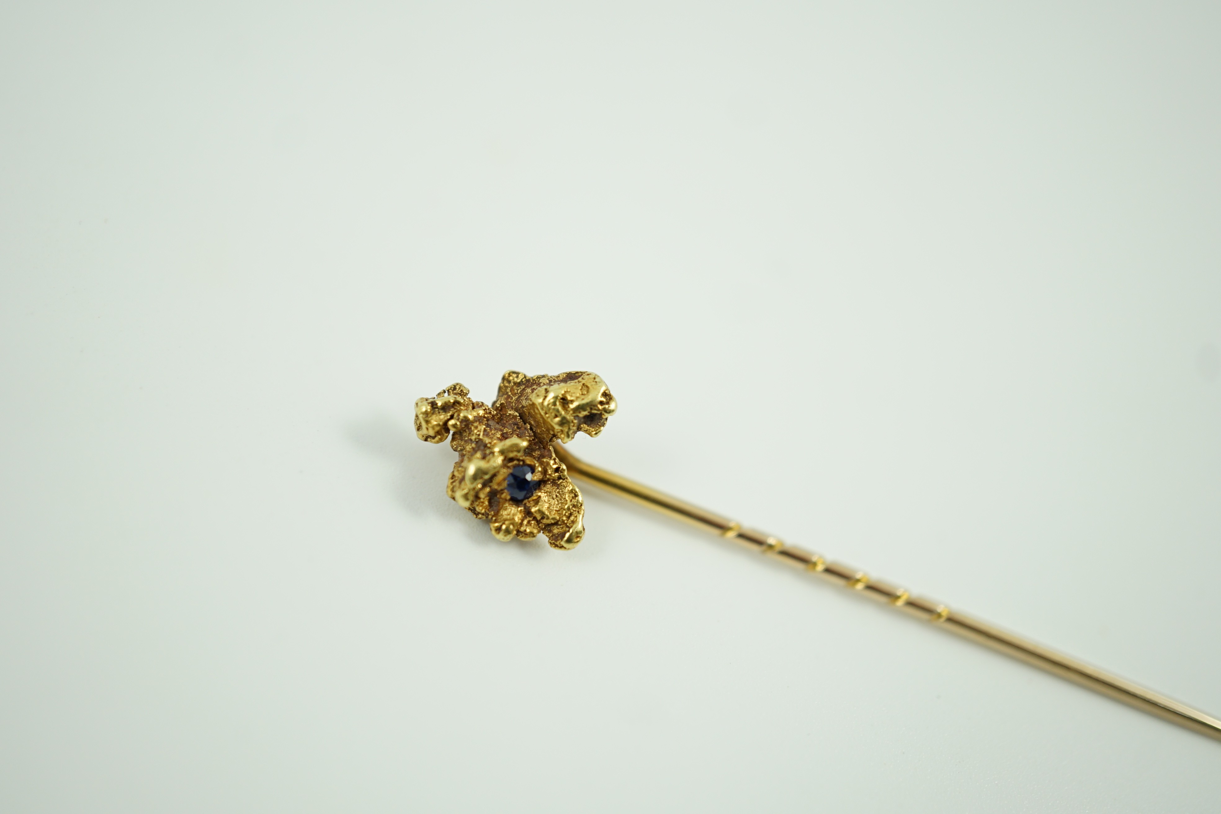 A late Victorian yellow metal and single stone sapphire set 'nugget' stick pin, 62mm, gross weight 3.2 grams.